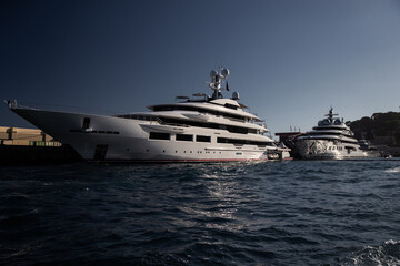 Two huge yacht in port of Monaco at sunset, glossy board of the motor boat, the chrome plated handrail, megayacht is moored in marina, sun reflection on glossy board, mountain is on background