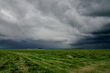 a foreboding dramatic dark grey thunder storm cloud sky over an open grass airfield and green meadows