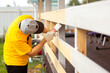 © Kiryakova Anna - A man in a bright yellow T-shirt and cap holds a brush in his hand and paints the boards on the porch of the house with white paint