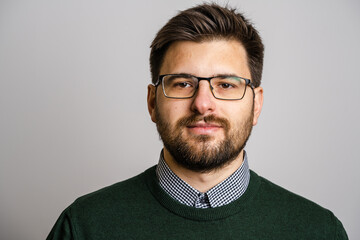 Portrait of one adult caucasian man 30 years old with beard and eyeglasses looking to the camera in front of white wall background wearing sweater young businessman success concept copy space