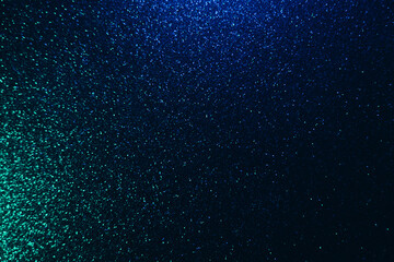 Wall Mural - Color glitter overlay. Blur sparkles. Bokeh light. Night sky stars reflection. Neon blue green grain texture glow on dark black shimmering abstract background.