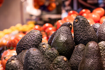 Closeup of some ripe avocados at the market stall with a some tomatoes with a blurred background