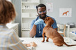 © Seventyfour - Young doctor of contemporary veterinary clinics examining sick dachshund sitting on table in front of him with pet owner behind
