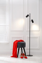 Sticker - Stylish ottoman with dress and floor lamp near white wall in room. Interior design