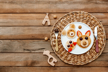 Wall Mural - Creative meal for a child, pancake with strawberry, funny food over wooden background. Top view, flat lay