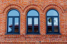Minimalistic Shot Of A Brick Wall With Windows. Three Arched Windows With Plastic Frame. Red Brick Masonry. Building A House Or Wall. Repeating Pattern