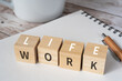 © ELUTAS - ワークライフバランスのイメージ｜「WORK」「LIFE」の積み木、ペン、ノート、コーヒーカップ