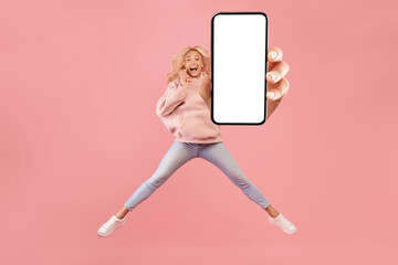 Full length of excited woman jumping and showing smartphone with empty space for mobile app or website on screen