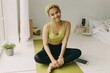 © shurkin_son - Toothy smiling African teenage blonde with curly shortcut in sportswear sitting on yoga mat in white stylish minimalistic room, legs crossed, pad with blank copy space for your advertisement on floor