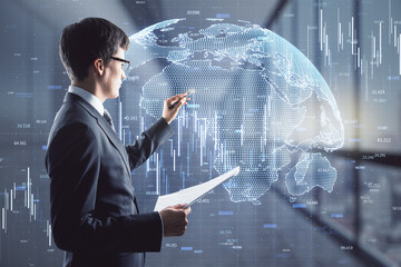 Poster - Attractive young european businessman with document standing in blurry office interior with abstract glowing globe and candlestick forex chart hologram. 