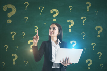 Poster - Portrait of attractive happy young european businesswoman with laptop standing on chalkboard wall background with question marks sketch. Solution and doubt concept.