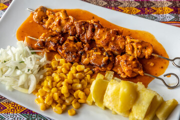 Sticker - A closeup shot of saucy barbeque with fried potatoes, corn, and onions on a white plate