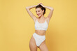 © ViDi Studio - Smiling minded attractive young brunette woman 20s wearing white underwear with perfect fit body standing ties hair in ponytail look camera isolated on plain yellow color background studio portrait