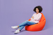 © ViDi Studio - Full body young smiling happy cheerful woman of African American ethnicity 20s wear pink striped shirt sit in bag chair look camera isolated on plain pastel light purple background studio portrait
