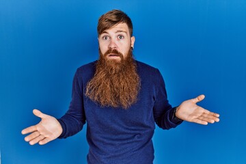 Canvas Print - Redhead man with long beard wearing casual blue sweater over blue background clueless and confused with open arms, no idea concept.