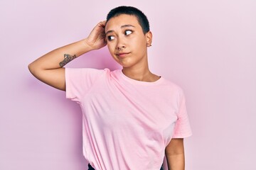 Poster - Beautiful hispanic woman with short hair wearing casual pink t shirt confuse and wondering about question. uncertain with doubt, thinking with hand on head. pensive concept.