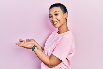 Sticker - Beautiful hispanic woman with short hair wearing casual pink t shirt pointing aside with hands open palms showing copy space, presenting advertisement smiling excited happy