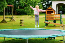 Little Preschool Girl Jumping On Trampoline. Happy Funny Toddler Child Having Fun With Outdoor Activity In Summer. Sports And Exercises For Children.