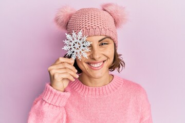 Canvas Print - Young brunette woman holding snowflake wearing winter cap looking positive and happy standing and smiling with a confident smile showing teeth