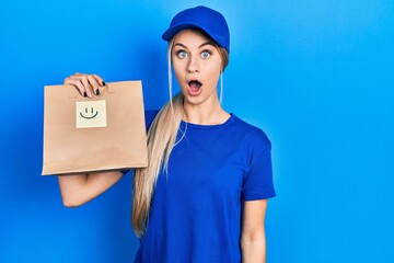 Canvas Print - Young caucasian woman holding take away paper bag with happy face reminder scared and amazed with open mouth for surprise, disbelief face