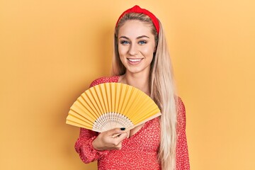 Poster - Young caucasian woman waving hand fan cooling air in summer looking positive and happy standing and smiling with a confident smile showing teeth