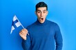 © Krakenimages.com - Handsome hispanic man holding finland flag scared and amazed with open mouth for surprise, disbelief face