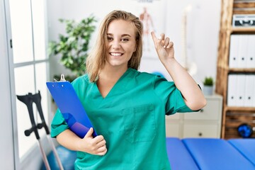 Poster - Young caucasian woman working at pain recovery clinic smiling amazed and surprised and pointing up with fingers and raised arms.