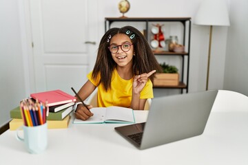 Sticker - Young african american girl doing homework at home with a big smile on face, pointing with hand finger to the side looking at the camera.