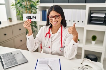 Canvas Print - Young hispanic doctor woman holding help banner smiling happy and positive, thumb up doing excellent and approval sign