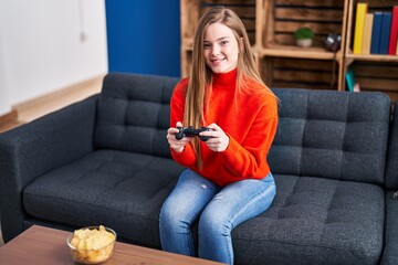 Poster - young blonde woman playing video game sitting on sofa at home