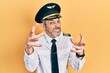 Handsome middle age man with grey hair wearing airplane pilot uniform shouting frustrated with rage, hands trying to strangle, yelling mad