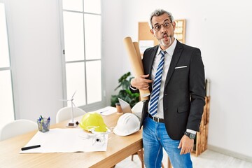 Poster - Middle age hispanic business man holding paper blueprints making fish face with lips, crazy and comical gesture. funny expression.