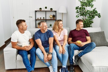 Wall Mural - Group of middle age people sitting on the sofa at home looking to side, relax profile pose with natural face and confident smile.