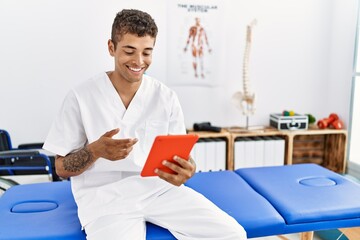 Sticker - Young hispanic man working as physiotherapist doing videocall at physiotherapy room