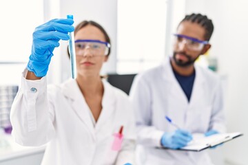 Wall Mural - Man and woman scientist partners holding test tube and writing on clipboard at laboratory