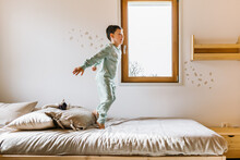 Cheerful Boy In Pajama Jumping On Bed