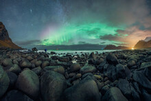 Anonymous Traveler Observing Aurora Borealis Over Sea From Rocky Beach