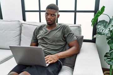 Canvas Print - Young african american man using laptop at home sitting on the sofa depressed and worry for distress, crying angry and afraid. sad expression.