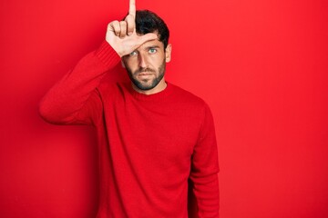 Poster - Handsome man with beard wearing casual red sweater making fun of people with fingers on forehead doing loser gesture mocking and insulting.