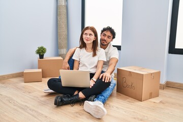 Wall Mural - Young couple using laptop at new home smiling looking to the side and staring away thinking.