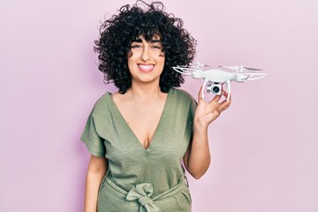 Sticker - Young middle east woman holding drone looking positive and happy standing and smiling with a confident smile showing teeth