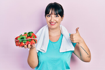 Sticker - Young hispanic woman wearing sportswear holding strawberries smiling happy and positive, thumb up doing excellent and approval sign