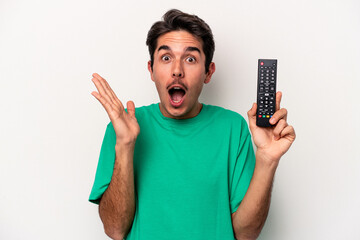 Young caucasian man holding a tv remote isolated on white background surprised and shocked.