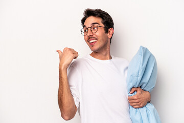 Wall Mural - Young caucasian man wearing pajamas holding a pillow isolated on white background points with thumb finger away, laughing and carefree.