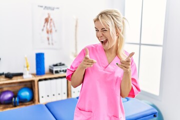 Poster - Young caucasian woman working at pain recovery clinic pointing fingers to camera with happy and funny face. good energy and vibes.