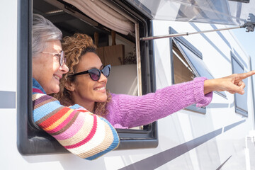 Portrait of attractive happy caucasian friends women traveling in camper van motor home looking out of the window. Caucasian couple of females enjoying free lifestyle, travel, vacation, freedom