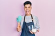 © Krakenimages.com - Young hispanic man holding bread dough and cooking tools sticking tongue out happy with funny expression.