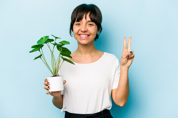 Young hispanic woman holding a plant isolated on blue background showing number two with fingers.