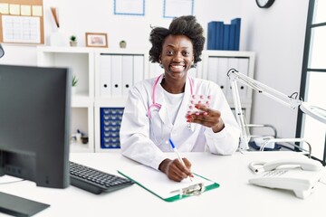 Young african american woman wearing doctor uniform holding pills at clinic