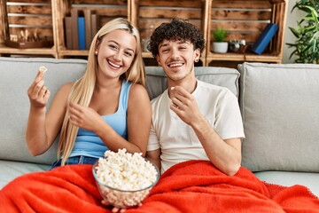 Poster - Young couple watching film and eating popcorn sitting on the sofa at home.